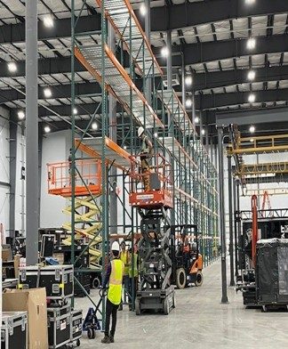 Install crew on scissor lifts assembling selective pallet rack with stage road cases staged on the floor